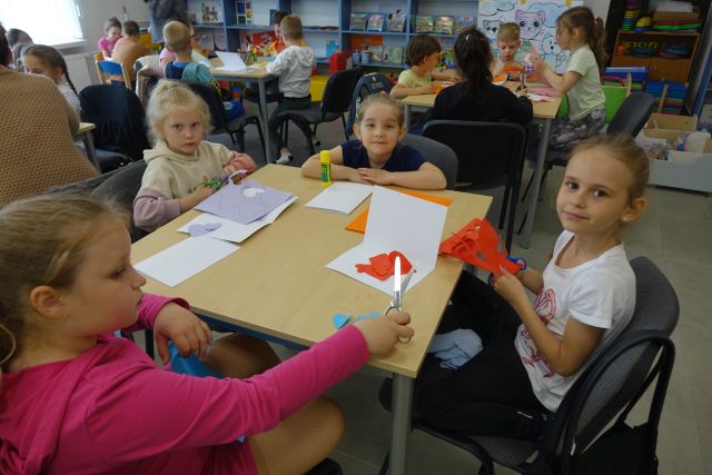 dzieci siedzą przy stolikach i wycinają serduszka