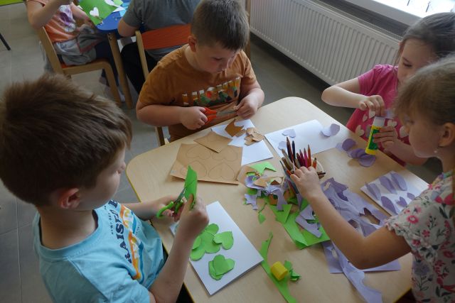 dzieci siedzące przy stolikach wycinają serduszka