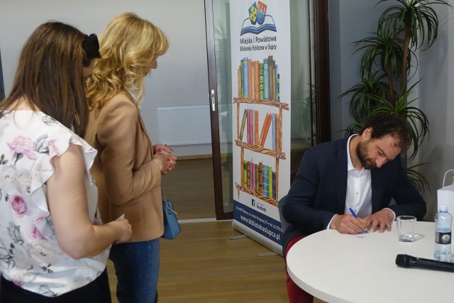 mężczyzna podpisuje się przed nim stojuą kobiety