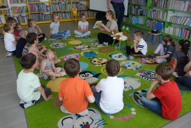dzieci uczestniczące w warsztatach siedzą z prowadzącą na kolorowym dywanie