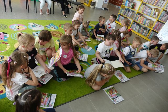 dzieci siedzą na zielonym dywanie i przegląda książki