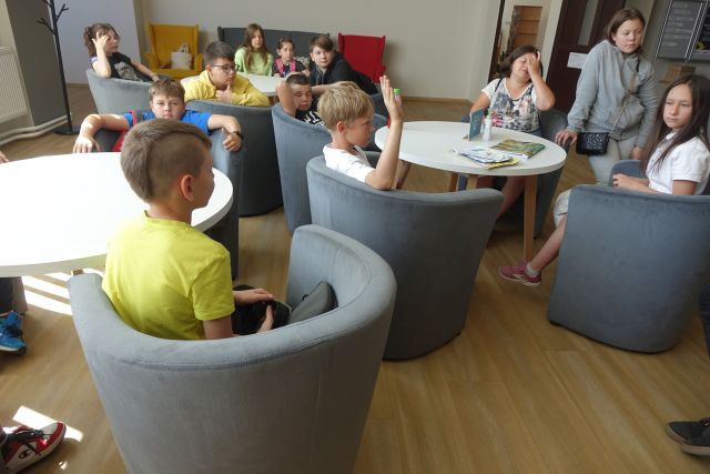 młodzież siedzi na siwych fotelach w czytelni biblioteki