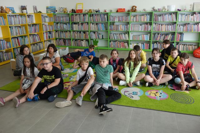 młodzież siedzi na kolorowym dywanie, w tle regały z książkami