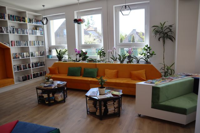 żółta sofa do siedzenia, przed nią małę stoliki z książkami