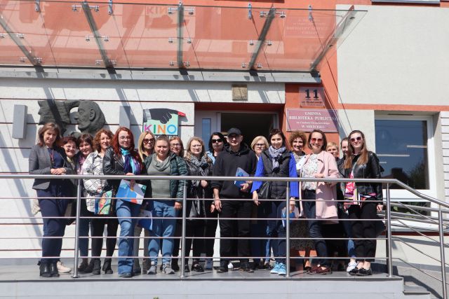 17 bibliotekarek i mężczyzna pozują do zdjęcia na tle schodach przed wejściem do biblioteki