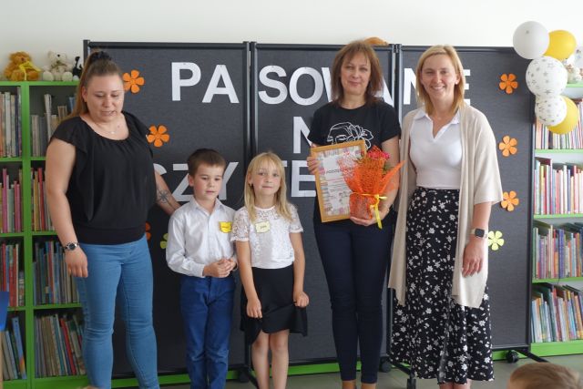 2 dzieci i 3 kobiety pozują do zdjęcia, jedna kobieta trzyma w rękach podziękowanie i kwiaty