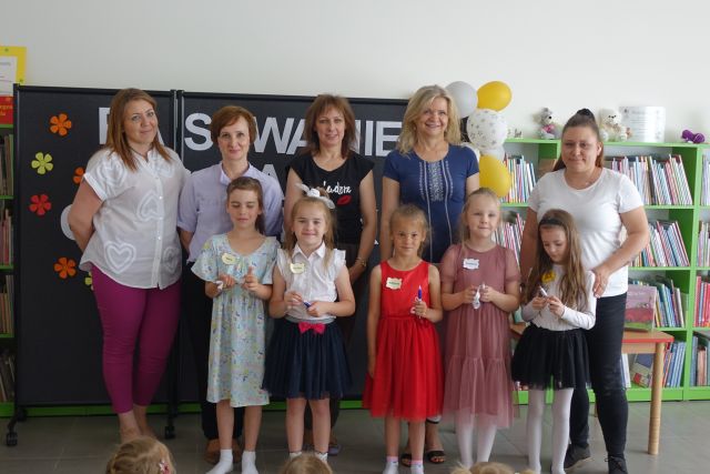 5 dzieci i 5 kobiet pozuje do zdjęciam w tle regały z książkami