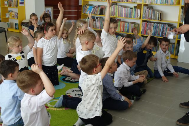 dzieci siedzą na dywanie z podniesionymi rękoma