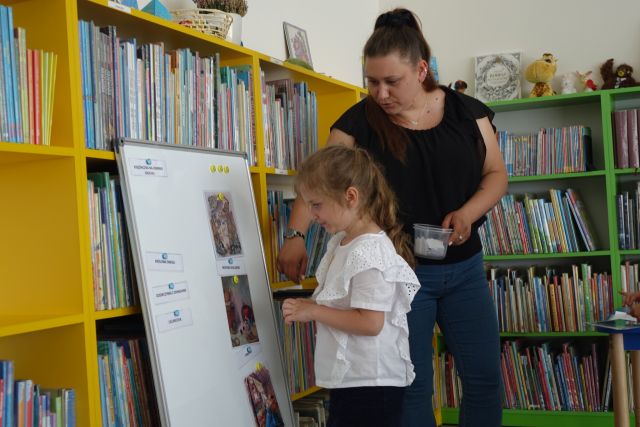 dziewczynka z ,obietą przypinają ilustracje z bajek do tablicy magnetycznej