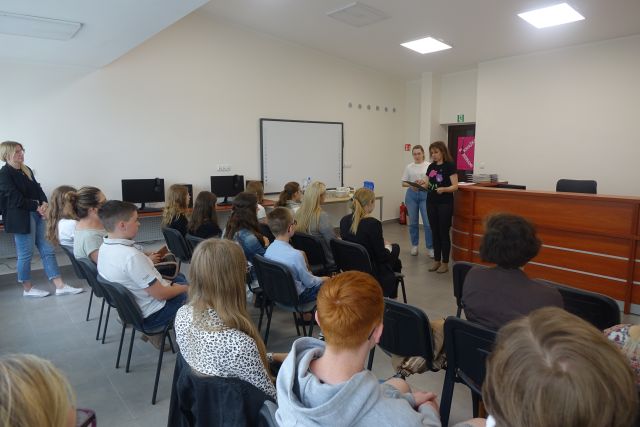 2 kobiety stoją przed uczestnikami konkursu siedzącymi na krzesłach