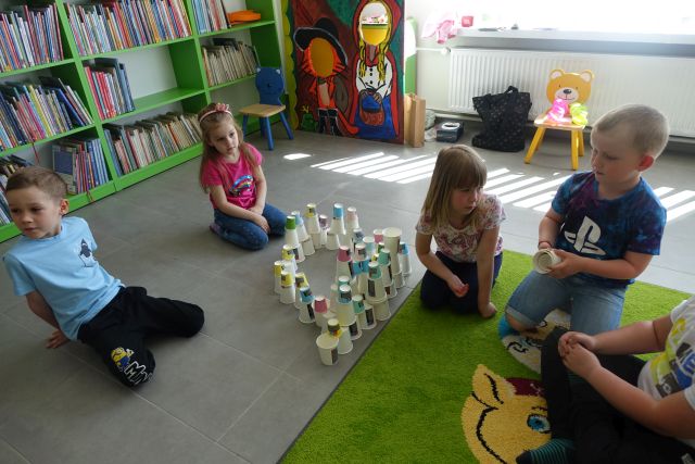 dzieci siedzą na podłodze i ukłądają plastikowe kubeczki