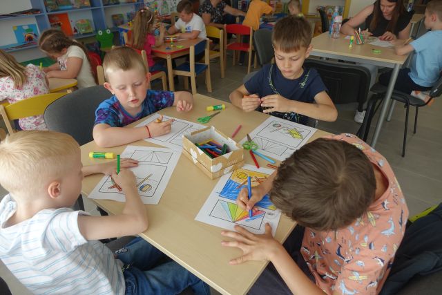 dzieci siedzą przy stołąch i rysują