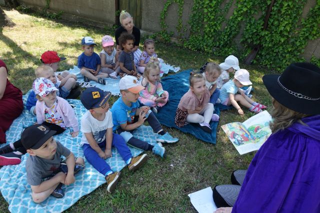 kobieta przebrana za kota w butach czyta dzieciom siedzącym na trawie książkę