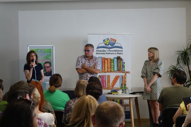 dwie kobie i pośrodku mężczyzna stoją przed siedzącą publicznością