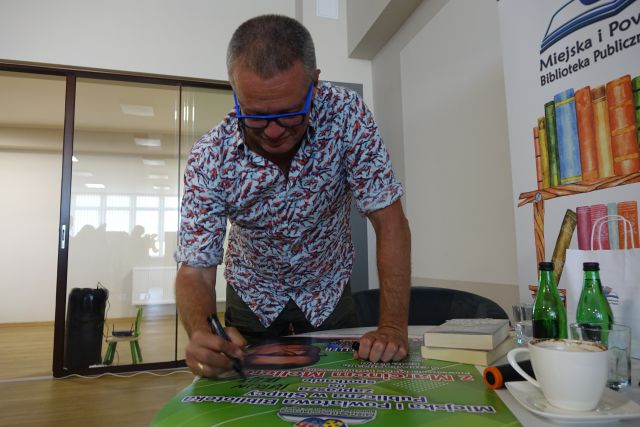 mężczyzna podpisuje plakat prezentujące jego z książkami