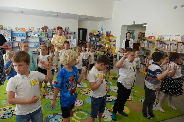 dzieci i przedszkolanki stoją i trzuymają w górze prawą rękę