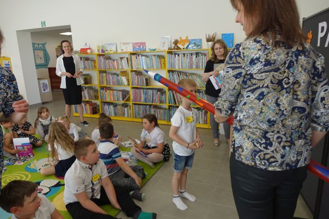 kobieta pasuje dużą kredką chłopca, inne dzieci siedzą na dywanie