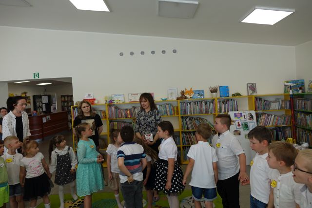 dzieci stoją przed dwoma kobietami , w tle regały z książkami