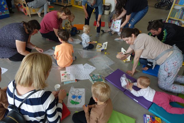 dzieci i rodzice siedzą na podłodze i malują farbkami
