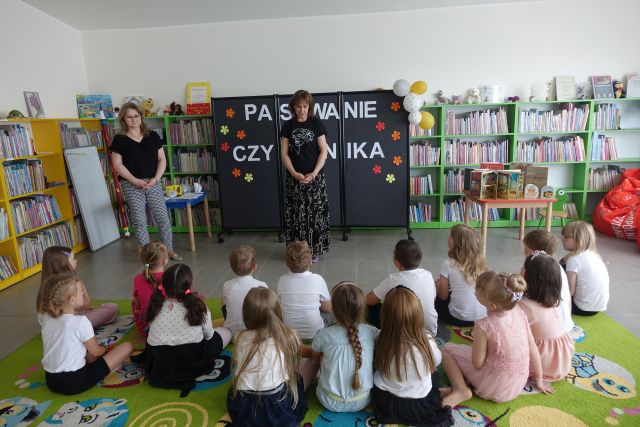 dwie kobiety stoją przed dziećmi siedzącymi na kolorowym dywanie