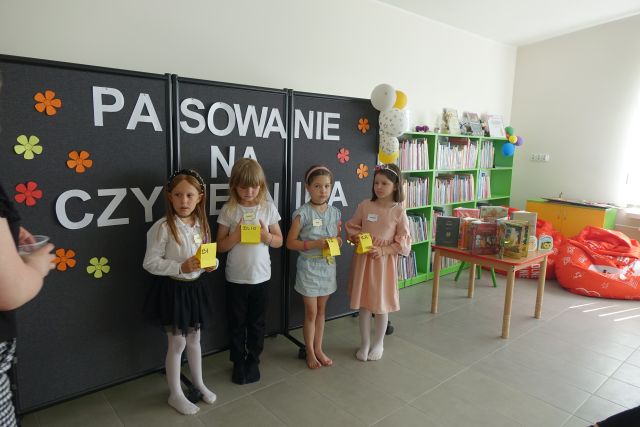 dzieci stoją z żółtymi karteczkami przed dziećmi siedzącymi na kolorowym dywanie