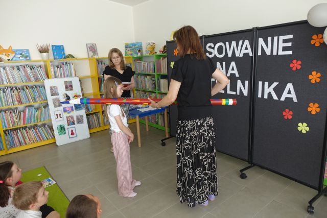 kobieta pasuje dziewczynkę ogromnym ołówkiem na czytelnika biblioteki