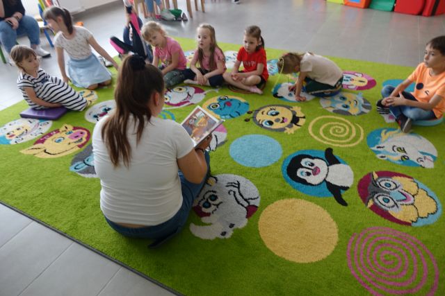 bibliotekarka czyta dzieciom siedzącym na kolorowym dywanie