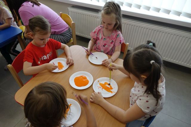 dzieci siedzą przy stoliku i maluchą na papierowych talerzykach