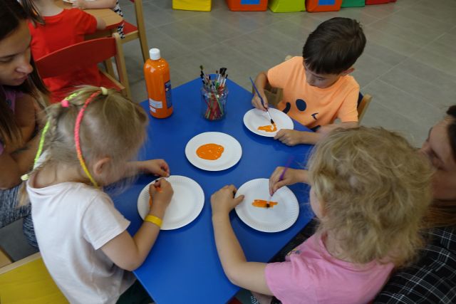 dzieci siedzą przy stoliku i malują na papierowych talerzykach