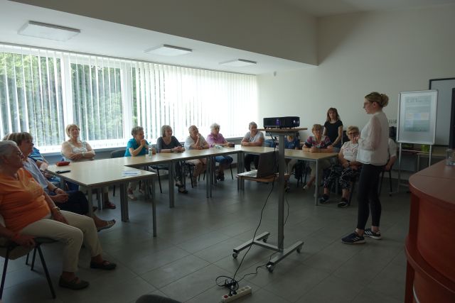 kobieta przemawia do siedzących seniorek