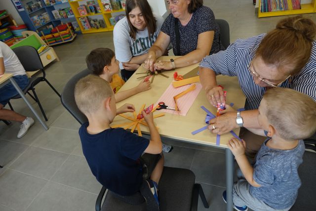 dzieci i rodzice siedzą przy stolikach i sklejają paski z papieru tworząc medale