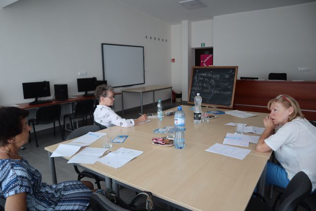 trzy kobiety siedzą przy stolikach na których leżą zeszyty i woda