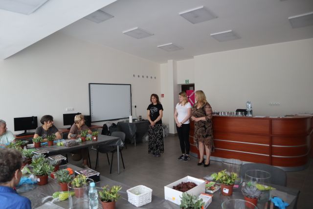 trzy kobiety stoją przed siedzącymi seniorkami w sali komputerowej