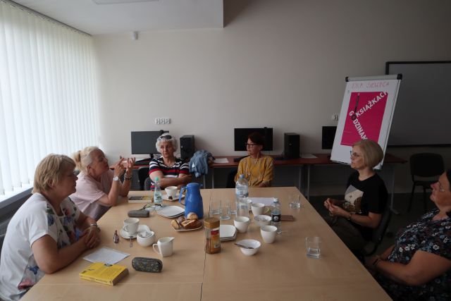 uczestniczki klubu czytelniczego siedząc przy stołach dyskutują o książkach