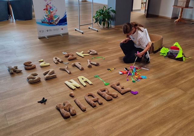 dziewczyna układa na podłodze uszyty z materiałów napis książka szyta na miarę oraz zakładki