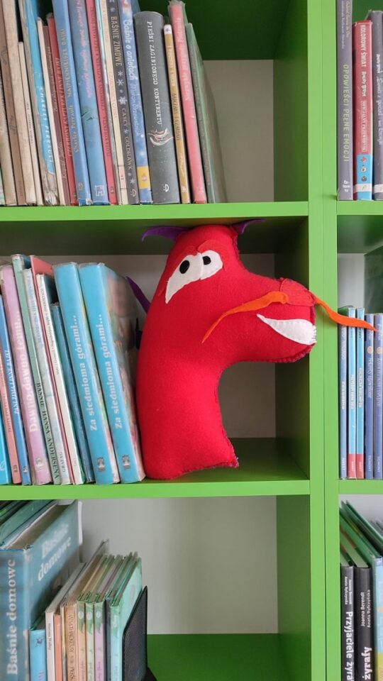 maskotka czerwonego psa na półce z książkami