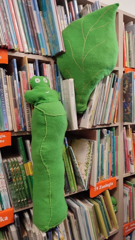 maskotka zielonej gąsienicy i liścia na półce z książkami