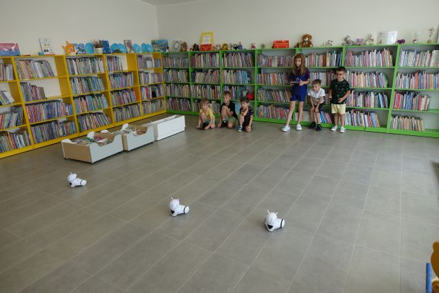 dzieci sterują robotami, w tle regały z ksiązkami