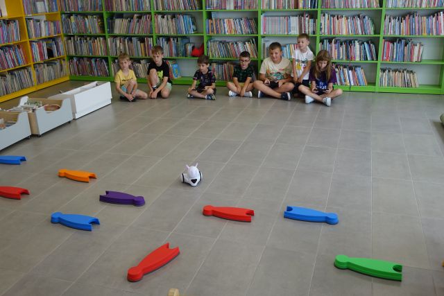 dzieci sterują robotami, w tle regały z książkami