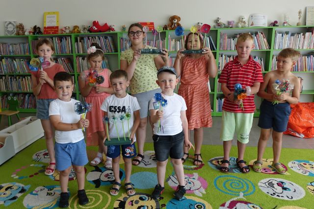 dzieci pozują do zdjęcia i pokazują wykonane przez siebie bukiety z plastikowych butelek, w tle regały z książkami