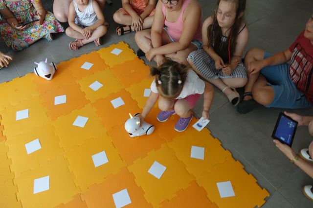 dzieci sterują przy użyciu tabletów robotami jeżdżącymi po pomarańczowej macie