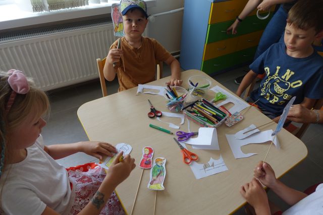 dzieci siedzą przy stole i wycinają pacynki