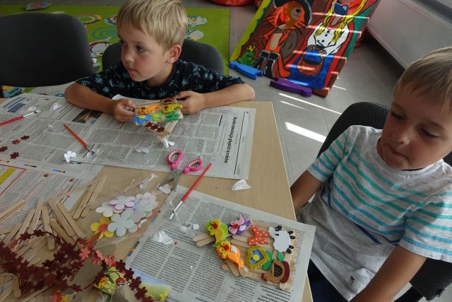 dzieci robią domki z patyczków i wyklejają je ozdobami z materiałów