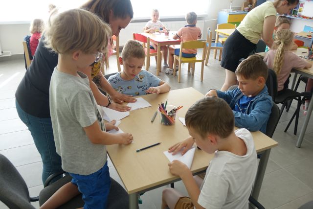 dzieci przy stolikach składają kartki papieru