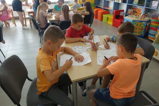 dzieci przy stolikach malują na kartkach