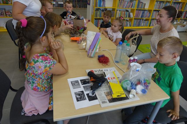 dzieci siedzą przy stolikach, przed nimi różne materiały recyklingowe