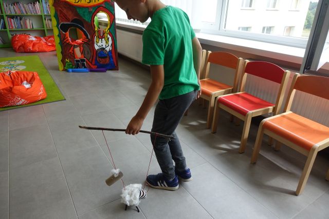 chłopiec pokazuje wykonaną przez siebie zabawkę z materiałó recyklingowych jak można nią sterować za pomocą nitek i kujka żeby chodziła