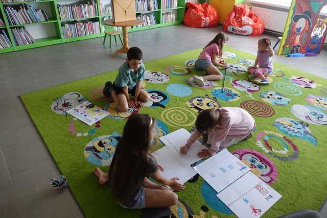 dzieci siedzą na kolorowym dywanie i wykonują ilustracje na białych kartkach