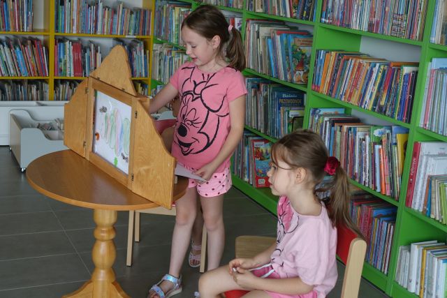 dwie dziewczynki pokazują ilustracje w teatrzyku kamishibai