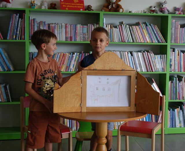 dzieci pokazują ilustracje w teatrzyku kamishibai